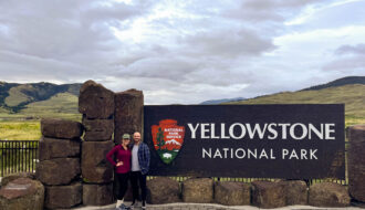 My husband and I standing next to the Yellowstone National park entrance sign at the north entrance